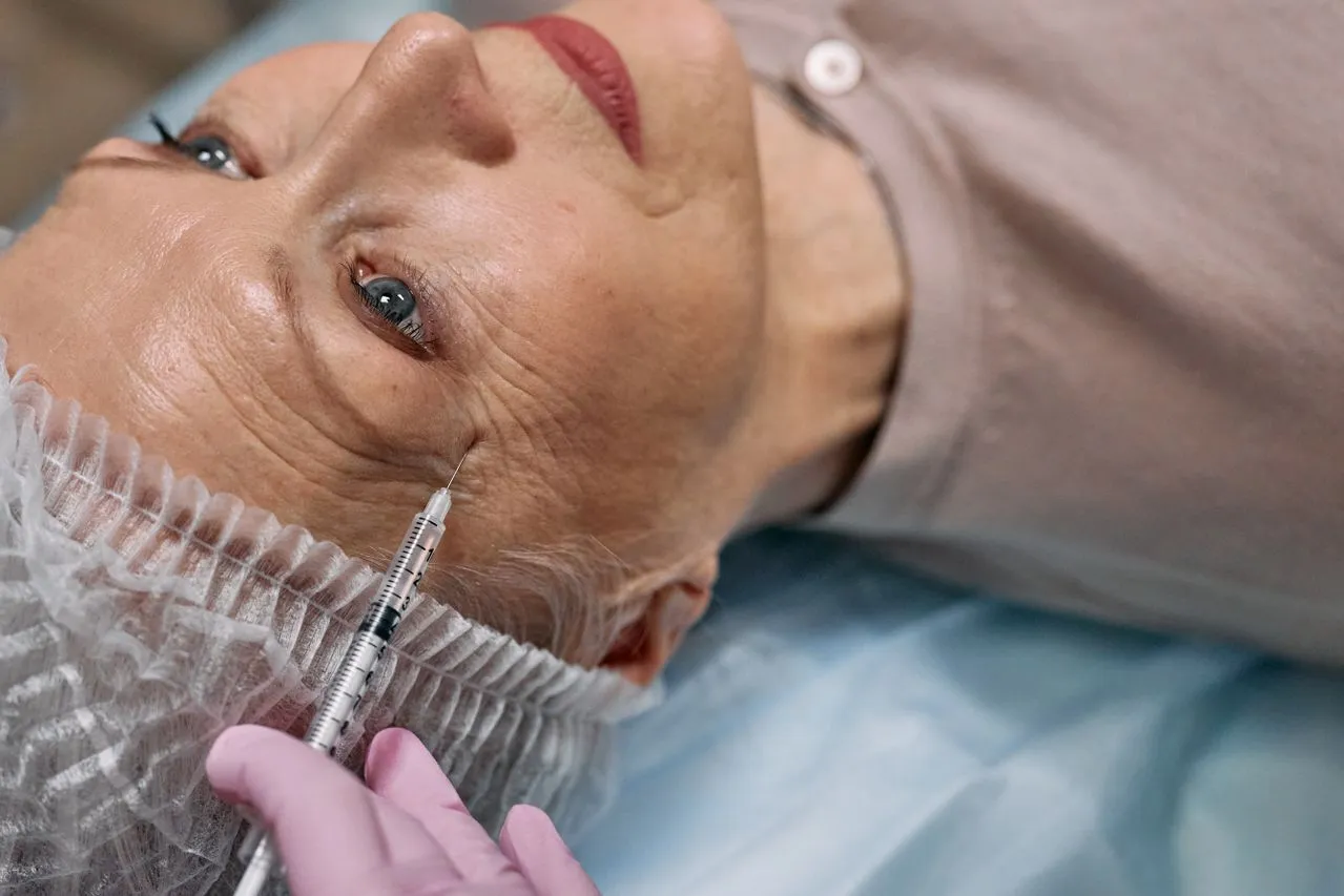 A senior woman receiving a filler injection near her eye at a medical clinic.